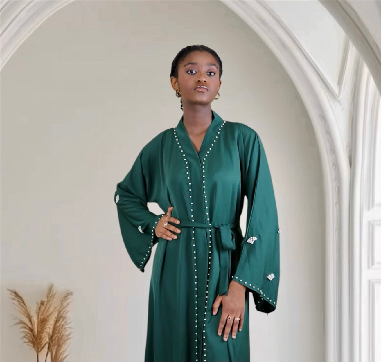 Woman wearing a green abaya with white embellishments in an elegant interior setting.