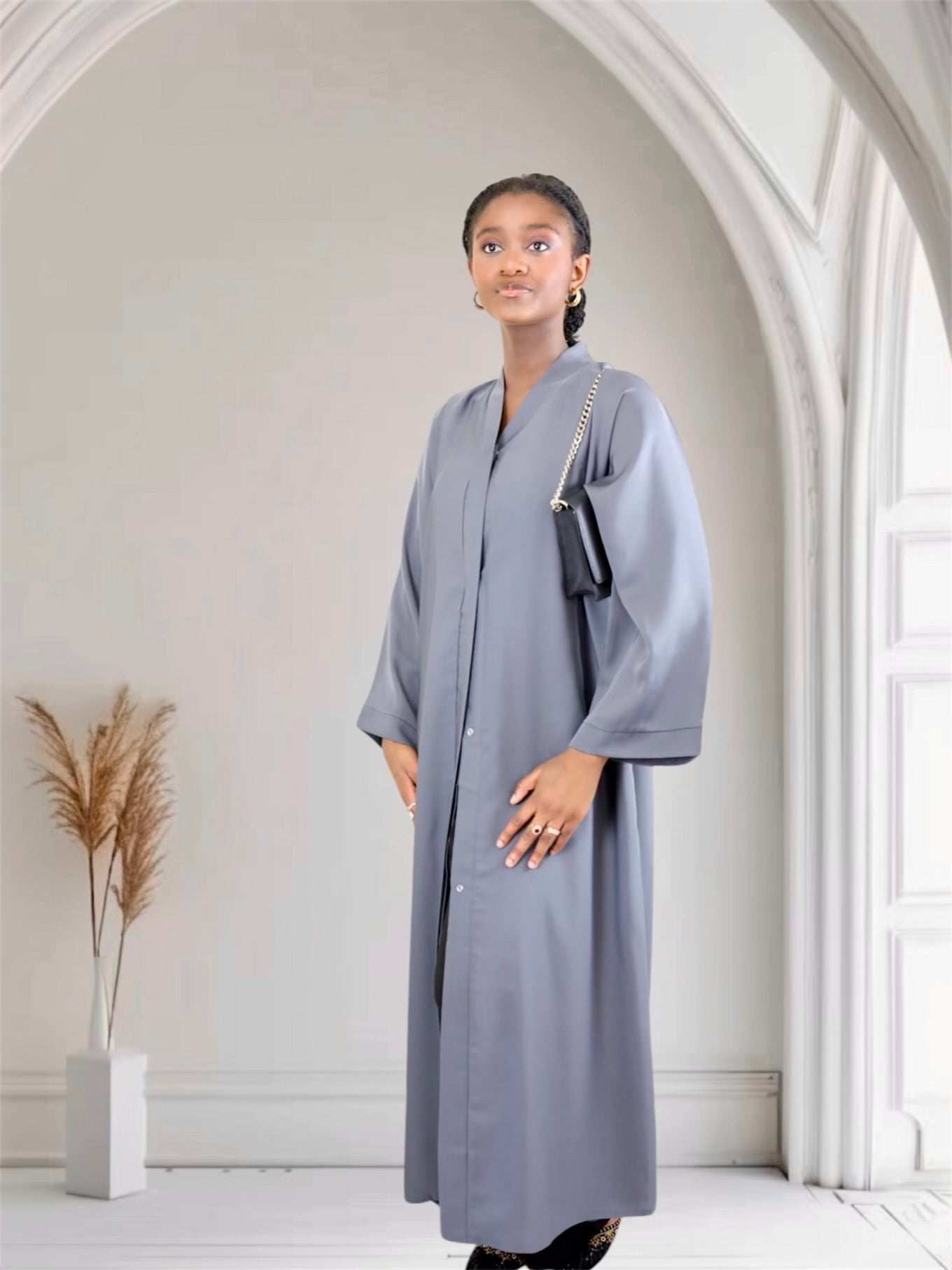 Woman wearing a long gray coat in a bright, minimalistic room.