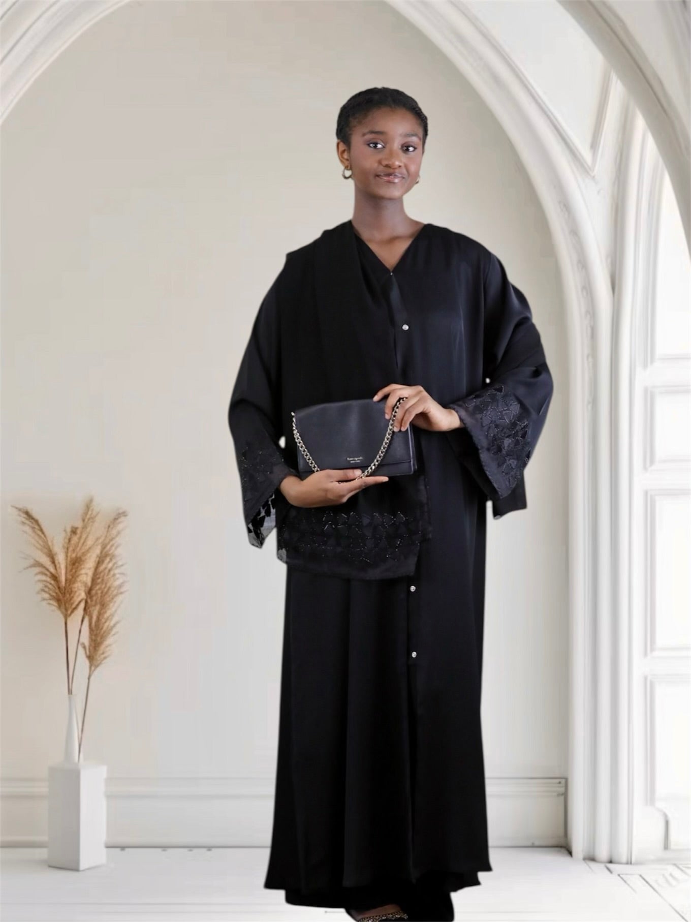 Woman holding a black handbag in a minimalistic indoor setting