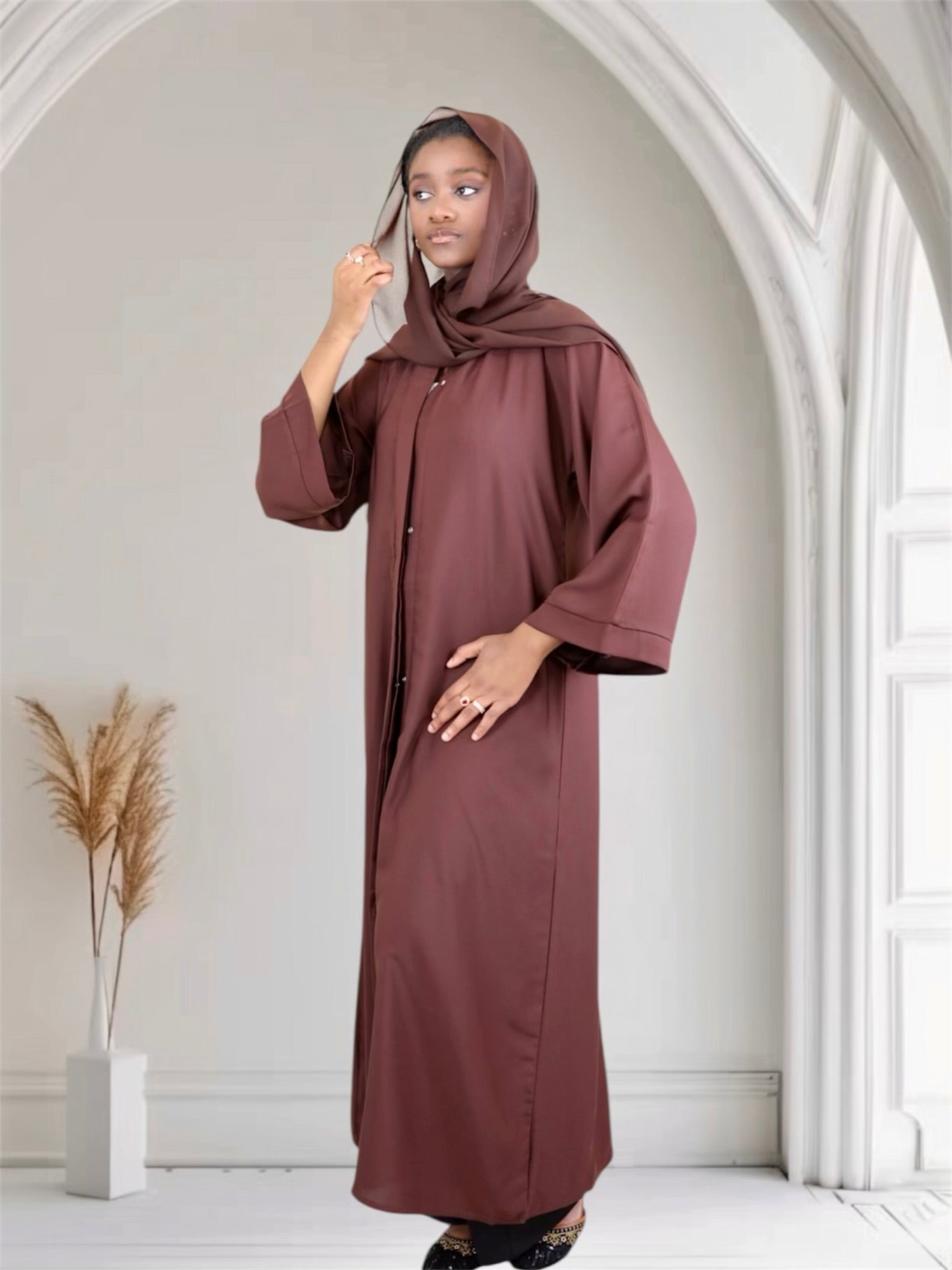 Woman wearing a long, brown abaya in a bright, minimalistic room.