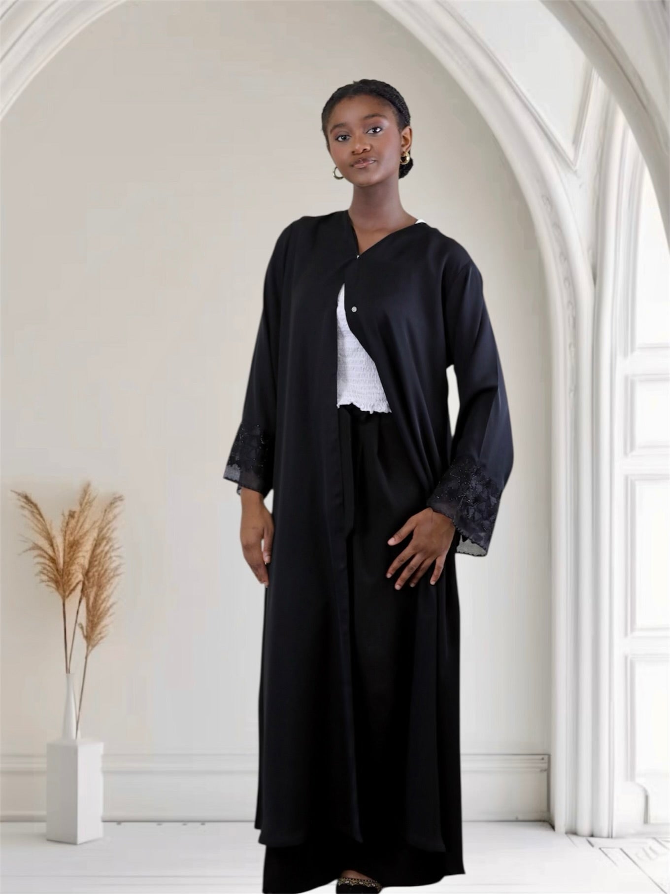 Woman wearing a black open front button-down abaya in a bright, minimalistic room.