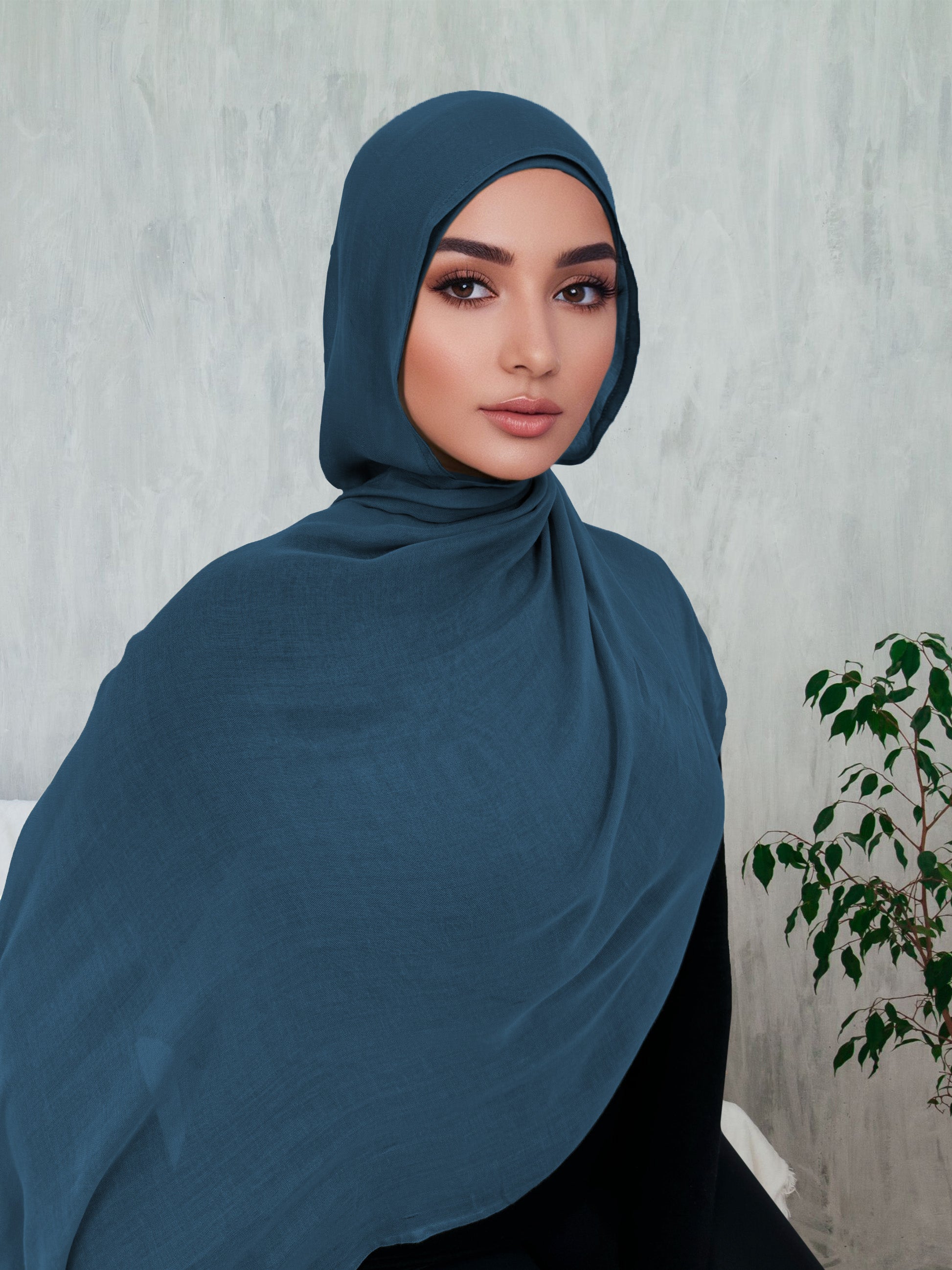 A woman wearing a teal blue modal hijab, draped over the head and shoulders.