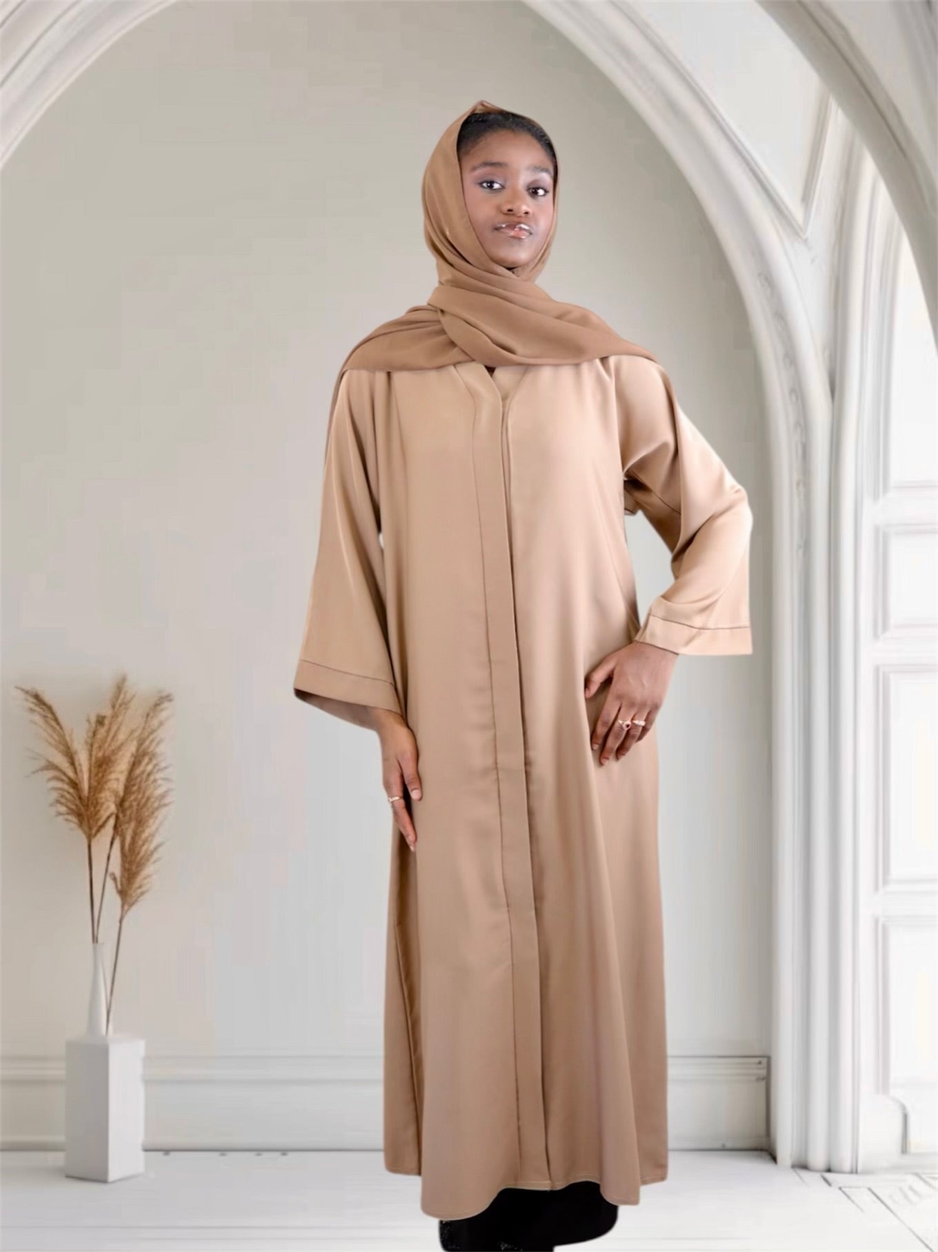 Woman wearing a camel brown abaya and hijab in a minimalistic room.