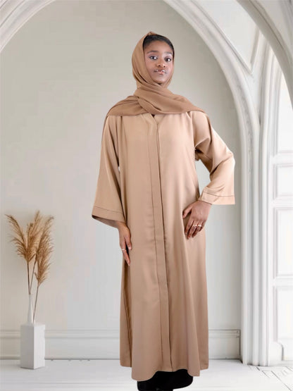 Woman wearing a camel brown abaya and hijab in a minimalistic room.