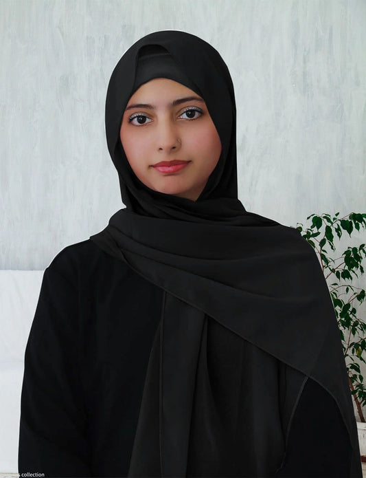 A woman wearing a black chiffon hijab, standing against a plain background.