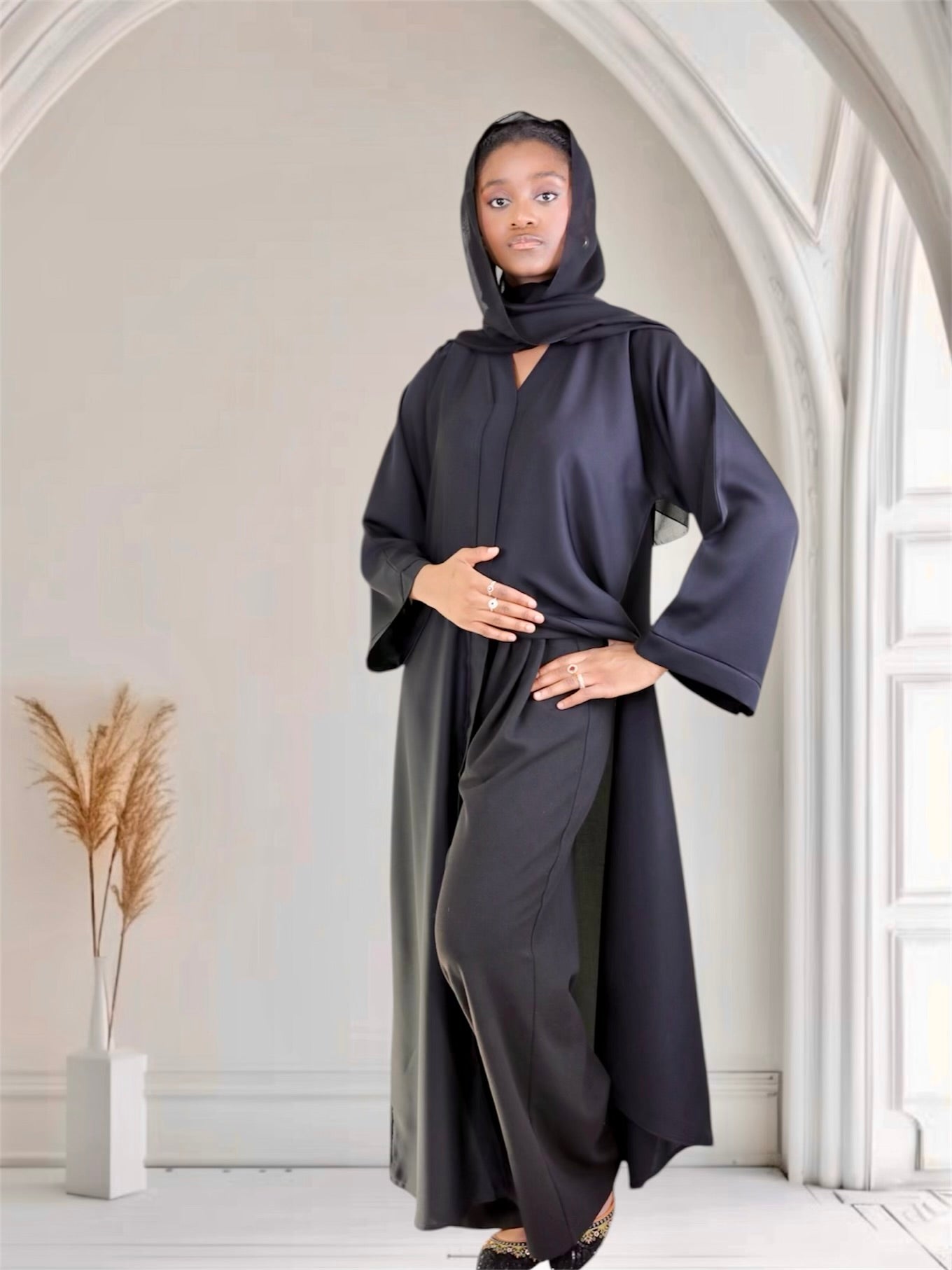 Woman wearing a long, dark gray hooded garment in a minimalistic room.