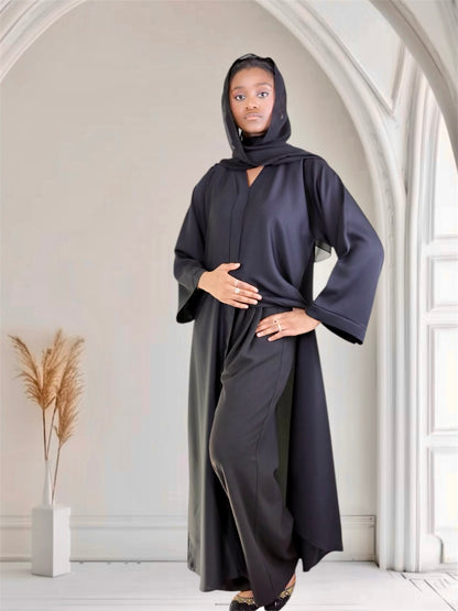 Woman wearing a long, dark gray hooded garment in a minimalistic room.