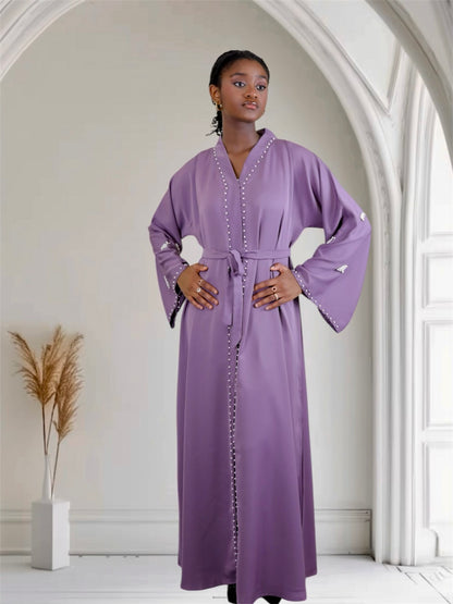 Woman wearing a long purple dress with white embellishments in a bright room.