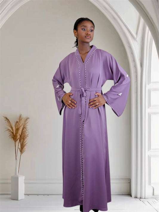 Woman wearing a long purple dress with white embellishments in a bright room.