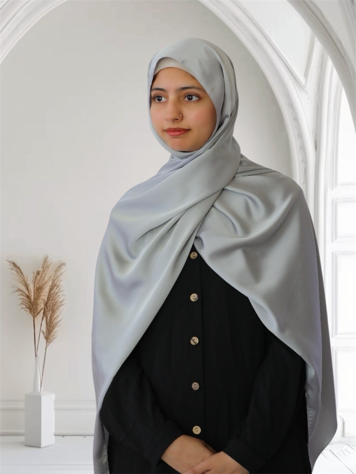 A woman wearing a silver gray satin silk scarf draped over her head and shoulders, with a black outfit.