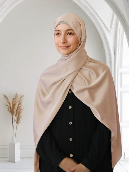 A woman wearing a light pink matte satin silk scarf draped over her head and shoulders, with a black outfit.