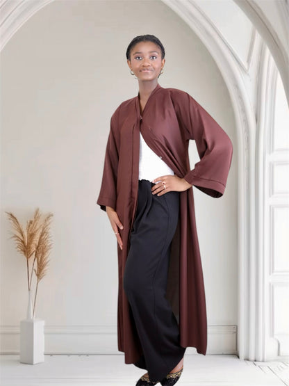 Woman wearing a long brown coat over a white top and black pants in a bright room.