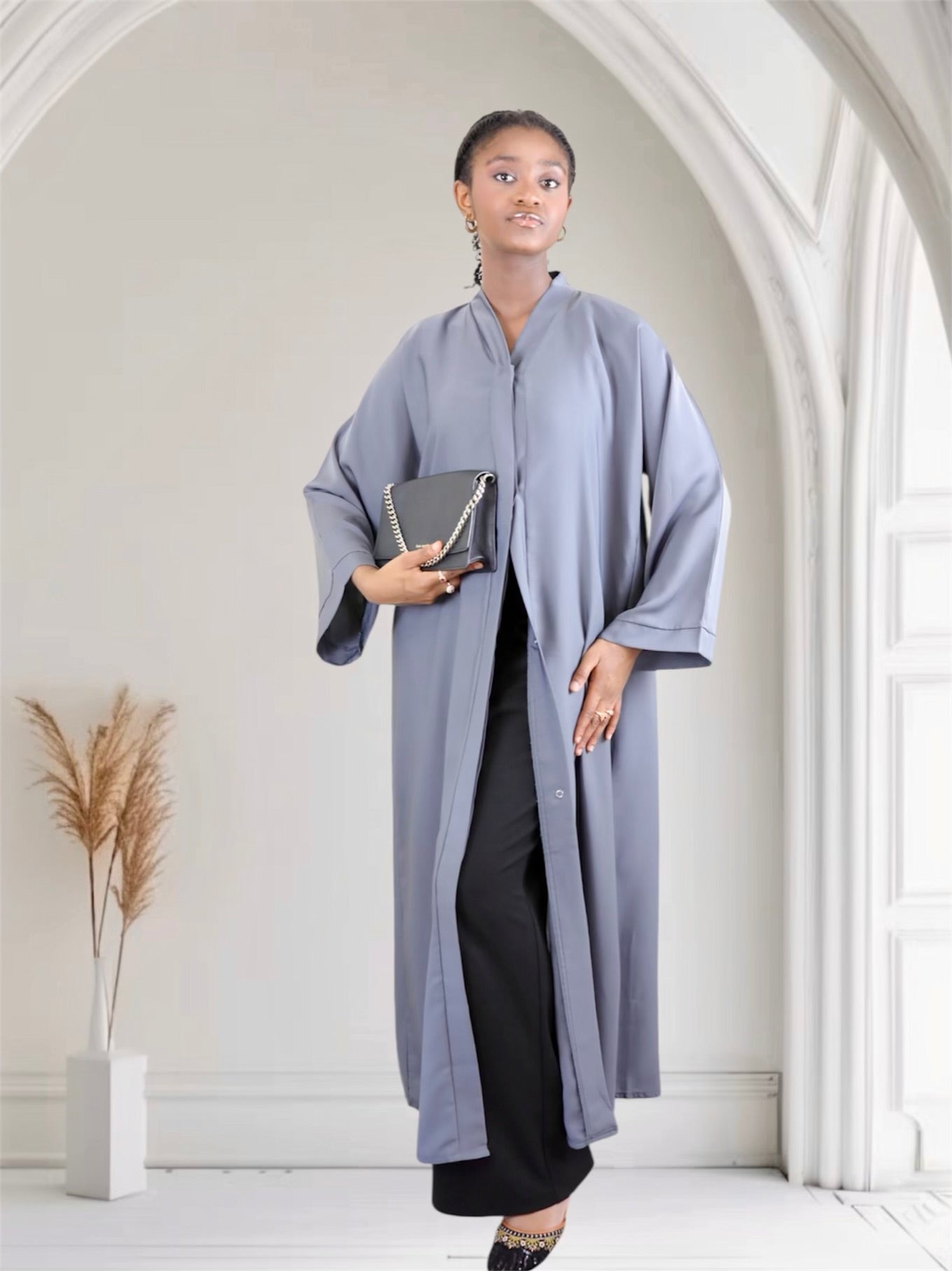 Woman wearing a long light gray abaya in a minimalistic room.