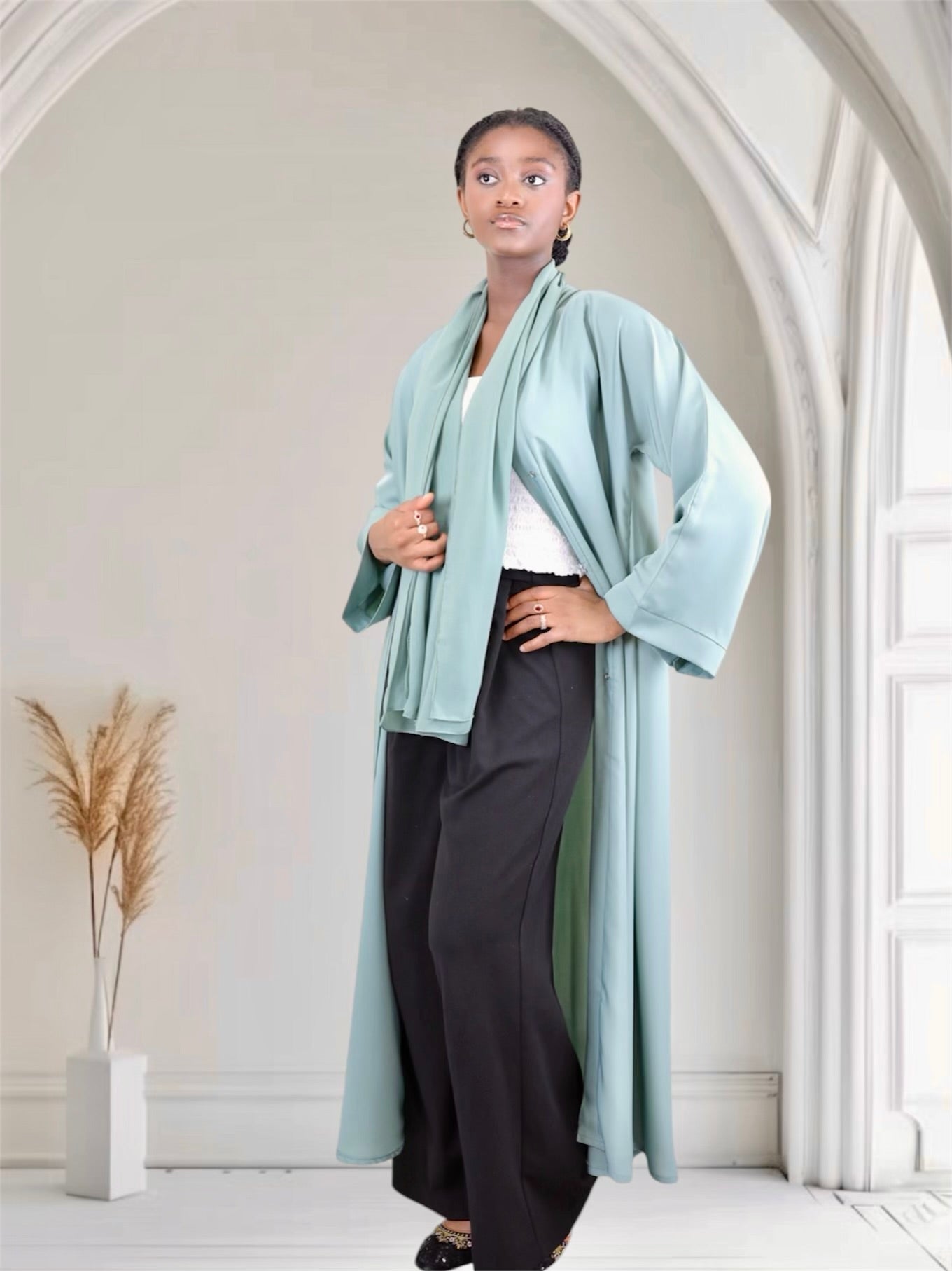 Woman wearing a light blue kimono-style garment in a minimalistic room.