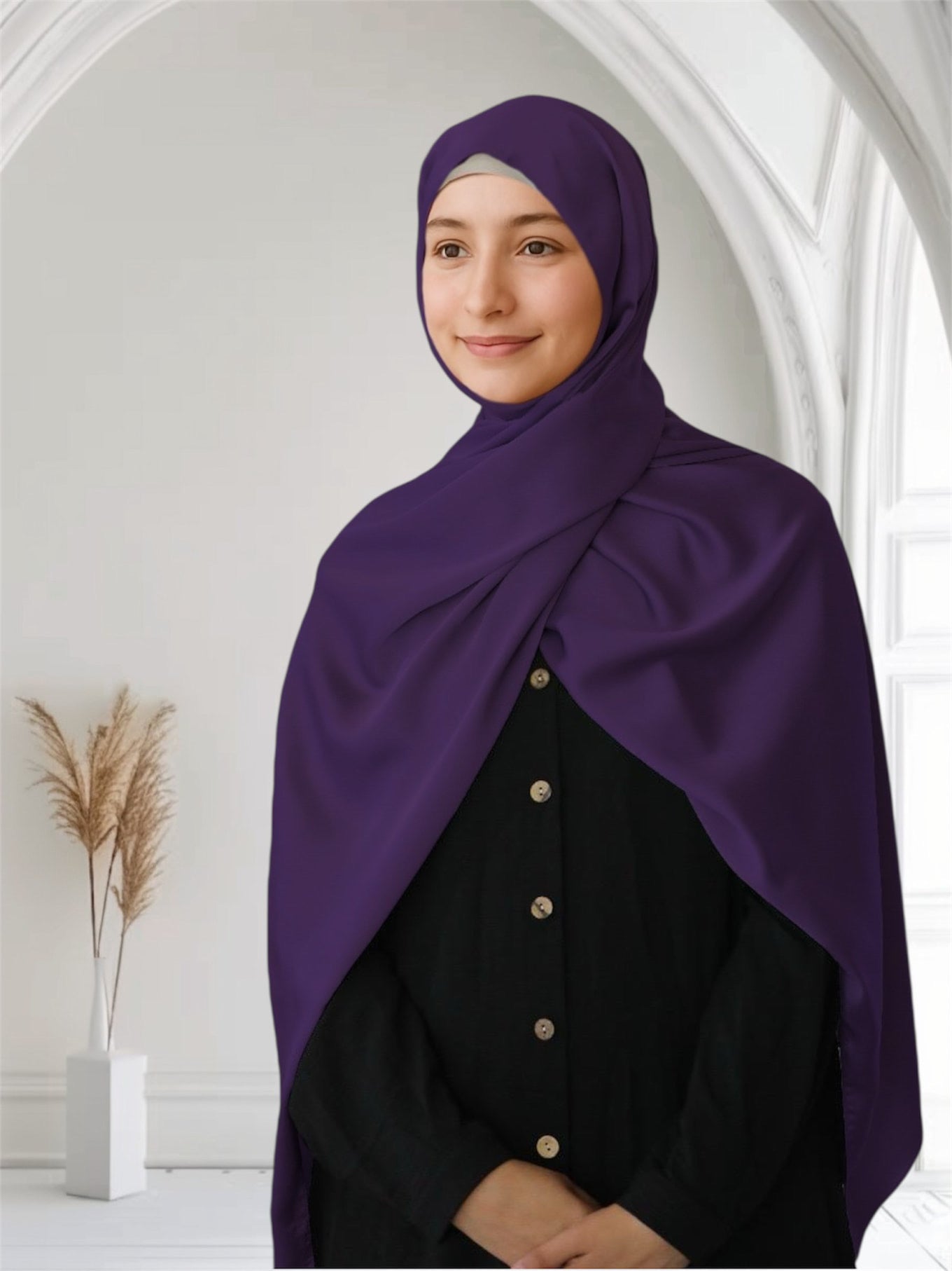 A woman wearing a plum purple matte satin silk scarf draped over her head and shoulders, standing in a room with a light background.